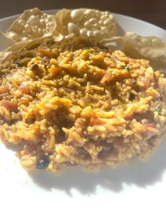 a white plate topped with rice and meat covered in sauce next to tortilla chips