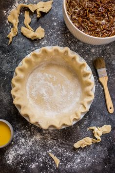 an uncooked pie crust next to a bowl of orange juice and a brush