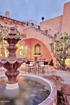 a fountain in the middle of a courtyard with tables, chairs and potted plants