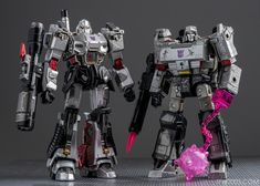 two toy robots standing next to each other in front of a gray background with red accents