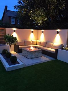 an outdoor living area with couches, fire pit and lights on the side of it