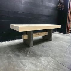 a wooden bench sitting on top of a cement floor next to a black wall in a building