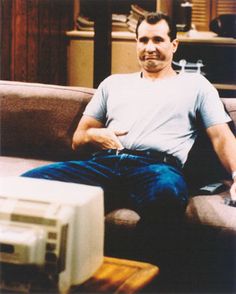 a man sitting on top of a couch next to an old computer monitor and keyboard