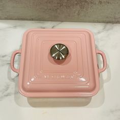 a pink tray with a metal lid on a marble countertop next to a white wall