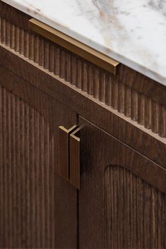 a close up of a wooden cabinet with marble top and brass hardware on the door