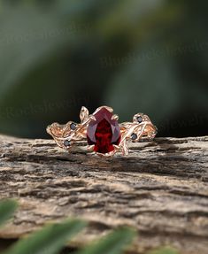 a red stone ring sitting on top of a piece of wood with leaves around it