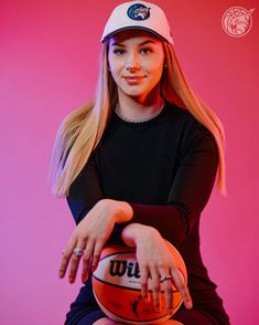 a beautiful young lady holding a basketball in her hand and posing for a photo with a pink background