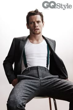 a man sitting on top of a wooden chair wearing a suit and white t - shirt