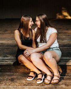 two young women sitting on the ground laughing and looking into each other's eyes