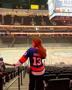 a woman standing in front of an empty ice rink at a hockey stadium with seats