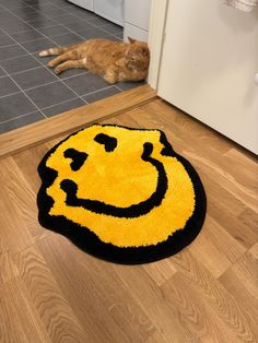 a cat laying on the floor next to a smiley face rug