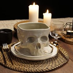 a table set for two with candles and a skull mug on it's plate