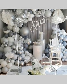 a table topped with balloons and flowers next to a wall covered in silver and white balls