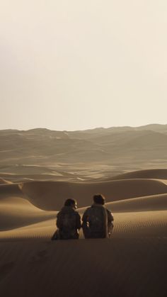 two people sitting on top of a sand dune