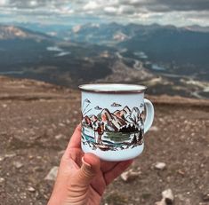 a hand holding a coffee cup on top of a mountain