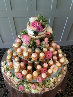 a three tiered cake with cupcakes and flowers on the top is displayed