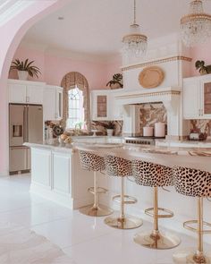 a kitchen with pink walls and marble counter tops, gold stools and chandeliers