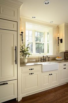 a kitchen with white cabinets and wood flooring next to an open doored window