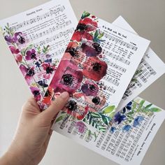 a person holding up three pieces of paper with flowers on them and music notes in the background