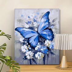 a blue butterfly painting on a wall next to a lamp and table with a plant