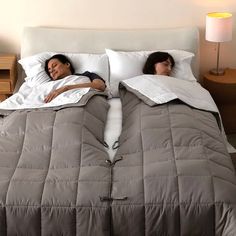 two women laying in bed with pillows and blankets