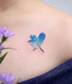 a small blue bird tattoo on the back of a woman's left shoulder and chest