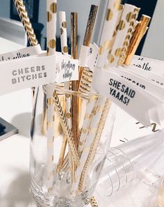 gold and white straws are in a clear glass vase on a table with tags