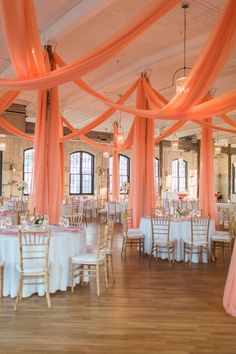 an indoor wedding venue with orange draping and white linens on the ceiling