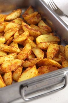 a pan filled with fried potatoes on top of a white countertop next to a knife and fork