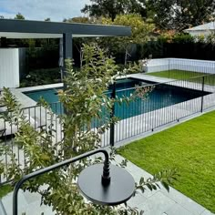 an outdoor swimming pool surrounded by lush green grass and trees, next to a white fence