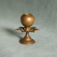 an antique brass candle holder with leaves on the top and bottom, sitting on a light blue background