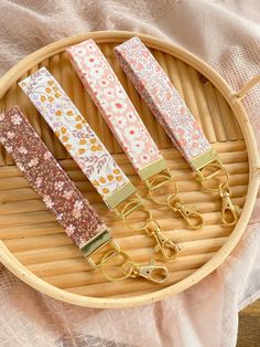 four keychains with flowers on them sitting in a bamboo basket next to a pair of scissors