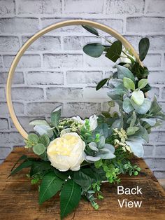 white flowers and greenery in a basket on a wooden table next to a brick wall