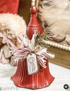 a red bell with a tag on it sitting on a table next to a christmas tree