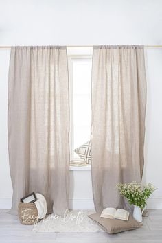 an open window with curtains and pillows on the floor in front of it, next to a potted plant