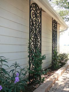 an iron gate on the side of a white house with purple flowers growing out of it