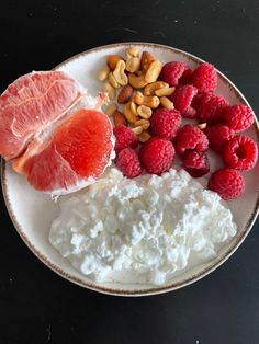 a white plate topped with fruit, nuts and yogurt next to raspberries