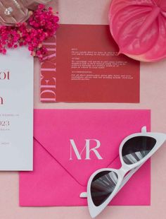 the wedding stationery is laid out on top of pink and red paper with sunglasses