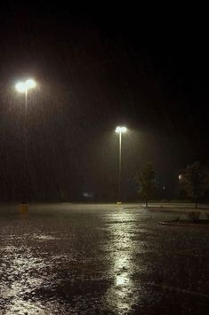 an empty parking lot in the rain at night with street lights and no one on it