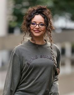 a woman with glasses is walking down the street wearing a gray shirt and black pants