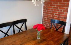 a wooden table with two black chairs and a vase filled with red roses on it