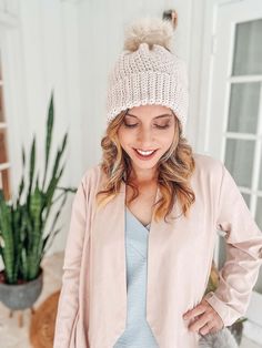 a woman standing in front of a potted plant wearing a white knit hat with pom - pom