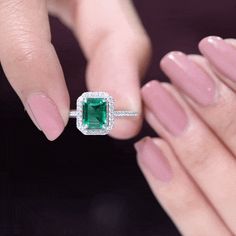 a woman's hand holding an emerald and diamond ring