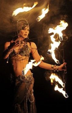 a woman with fire in her hands and headdress on, holding two torches