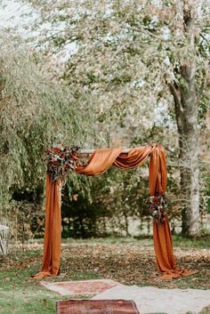 an outdoor wedding ceremony with orange draping and flowers on the arch, surrounded by trees