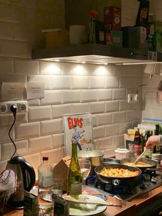 a woman cooking food on top of a stove next to a bottle of wine and an oven