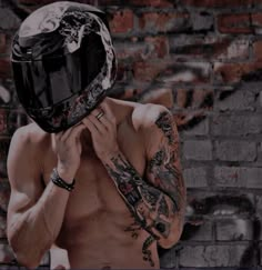 a shirtless man wearing a motorcycle helmet standing in front of a brick wall