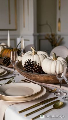 a table set with white pumpkins and gold place settings