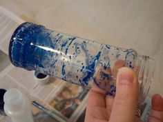 a person holding a blue and white water bottle in their left hand, with paint splattered on it