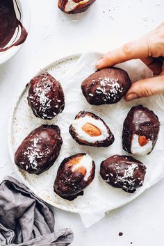 chocolate covered desserts on a white plate with someone picking up one from the plate